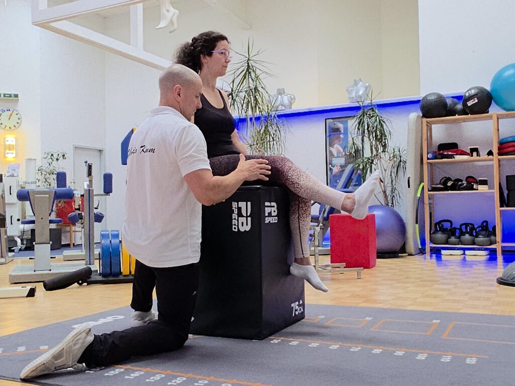 Therapeut begleitet eine Patientin bei einer Beinübung auf einer Trainingsbox.