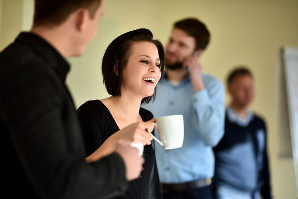 Eine Frau unterhält sich mit drei Männern bei einer Kaffeepause in beruflicher Umgebung
